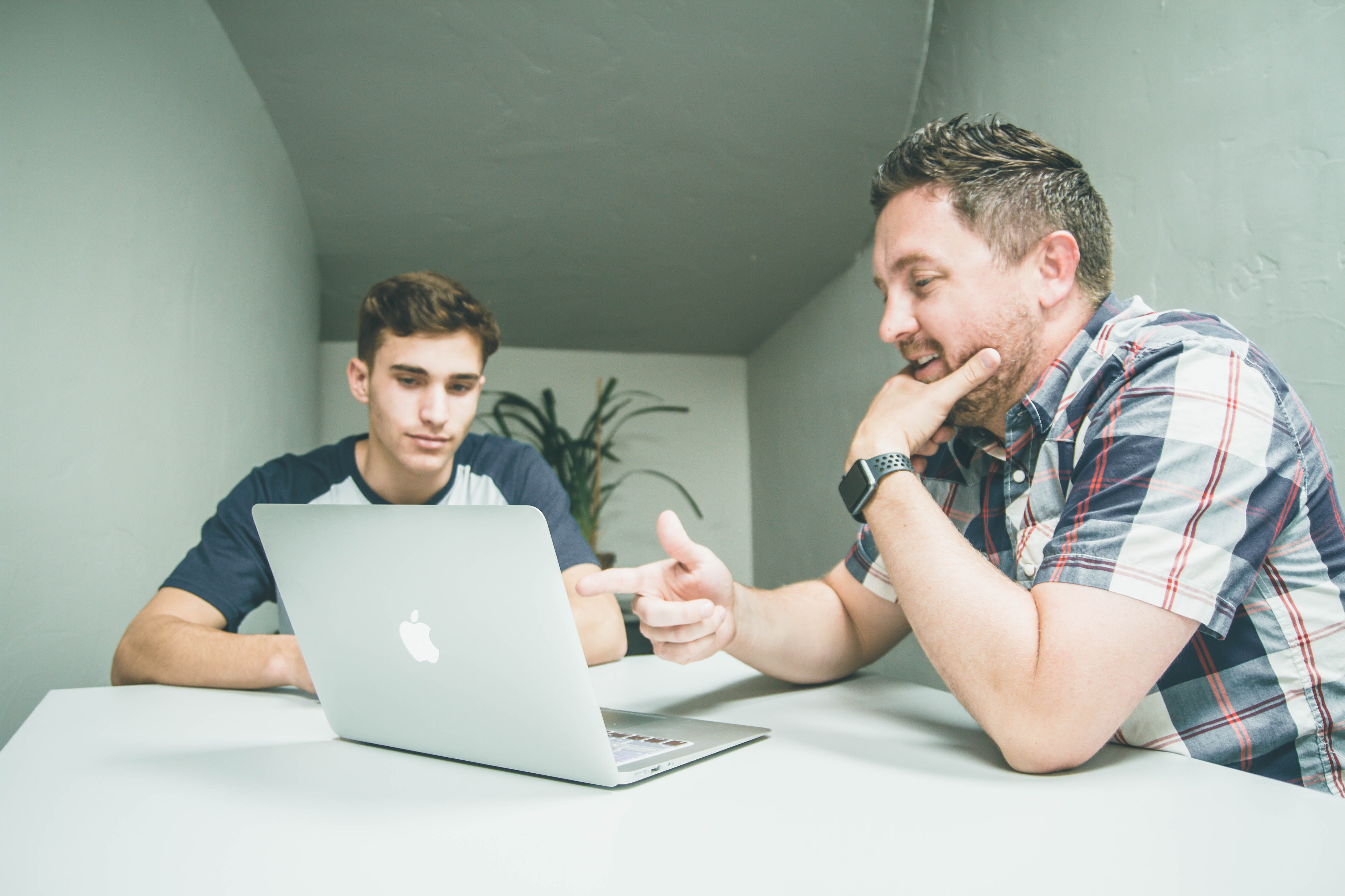 man-in-blue-and-white-shirt-explains-something-to-another-man-silver-macbook
